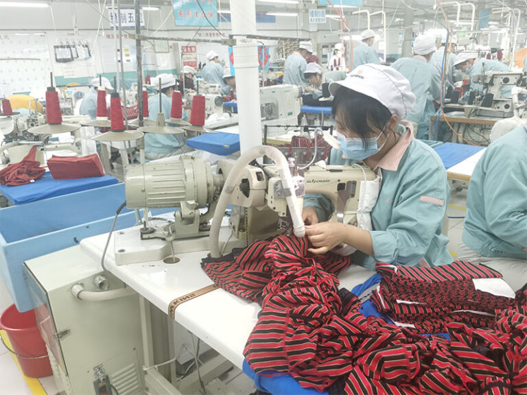Generic production scene from the official About page: a sewing workshop with workers at machines. No company marking is